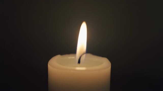 White candle flame flickering gently in a dark room