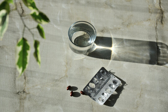 Glass of water and medication pills with plant shadows on stone surface