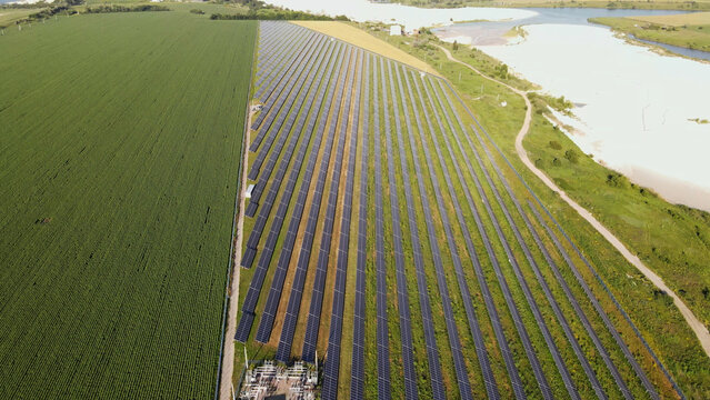 Aerial view of solar farm producing clean energy next to agricultural field and natural landscape, illustrating sustainability