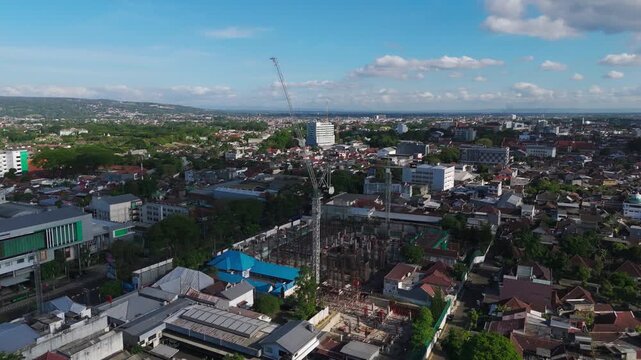 Malang, Indonesia - 23 July 2026: Aerial view of hotel building construction site with a tall crane amidst the urban landscape.