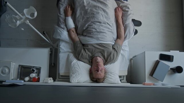 Caucasian young adult man lying in hospital bed with bandaged arm, with closed eyes. Footage for medical insurance, patient recovery, and healthcare services commercials