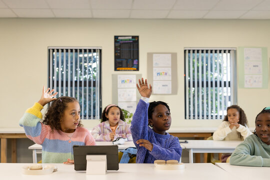 African American teenage female students raising hands around tablet and notebooks in classroom