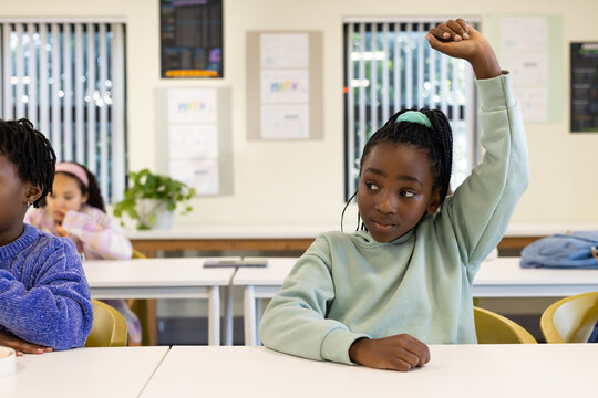 African American schoolgirls sitting at school desks, girl in green sweatshirt raising right hand