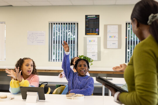 African American teacher holding tablet at school, teenage girl in purple sweater raising hand