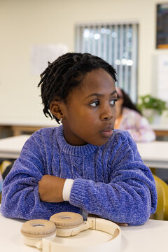 African American youth female student sitting at classroom desk wearing blue sweater beige headset