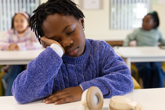 African American female children in classroom, front child sleeping in blue sweater, beige headset