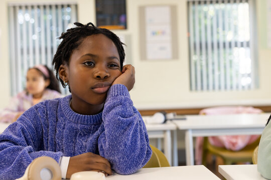African American child sitting in classroom in purple sweater resting chin, headphones on desk