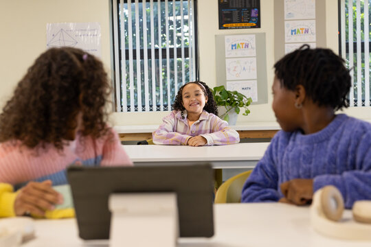 African American teenage girls sitting at desks in class, centered student smiling with tablet