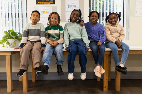 African American schoolchildren sitting on wooden bench in classroom with MATH posters
