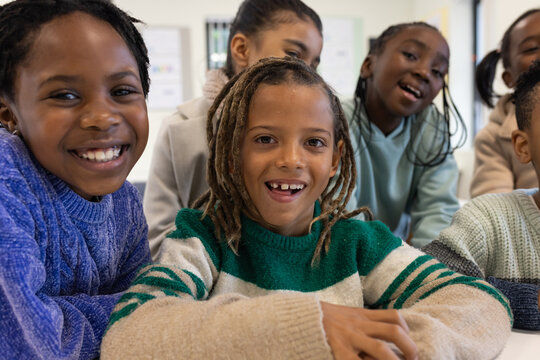 African American youth classmates leaning in at classroom table, smiling and wearing knit sweaters