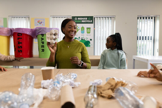 African American female instructor and female youth holding egg carton and sorting bottles in room