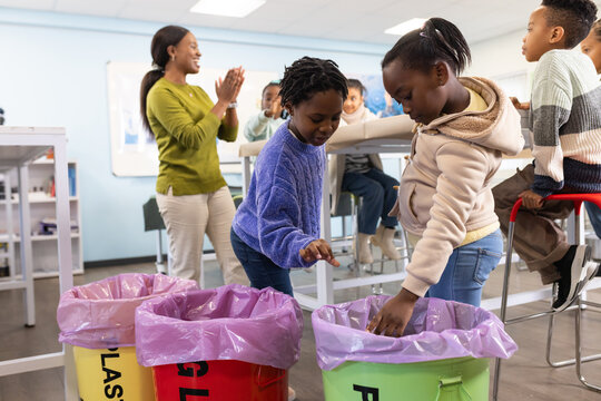 African American teacher guiding child students sorting recycling into purple-lined bins at school