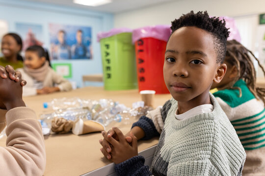 School group, African American boy in gray sweater sorting bottles by PAPER GLASS bins, copy space