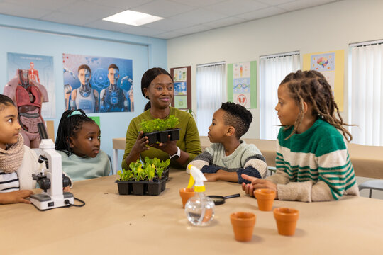 African American teacher with 4 students holding seedling tray, explaining in lab with microscope