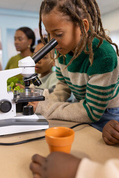 African American children leaning and viewing microscope, petri dish while teacher watching nearby
