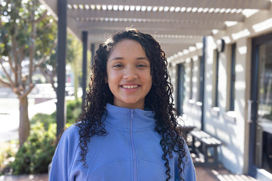 African American teenage woman standing under pergola path wearing light blue zip-up fleece jacket