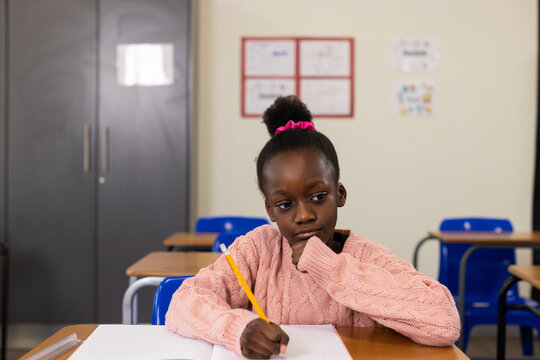 Child girl sitting at school desk wearing sweater writing on paper with yellow pencil ruler