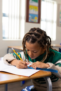 African American boy drawing with yellow pencil and blue ruler on open notebook at school desk