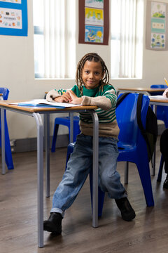 African American school-age boy sitting in classroom at desk writing in notebook with pencil