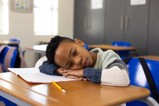 African American child student sitting resting head on hands at classroom desk with open notebook