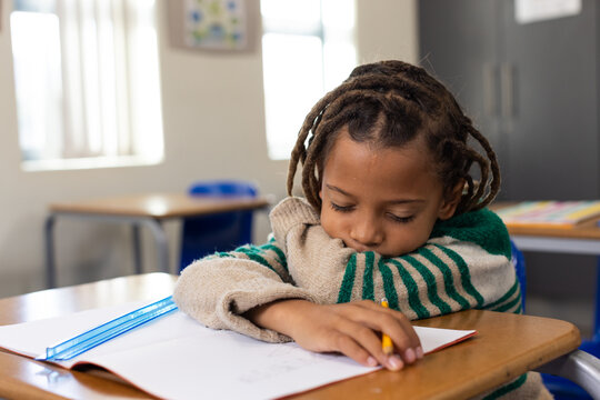 African American child resting on desk holding pencil over notebook in classroom with blue ruler