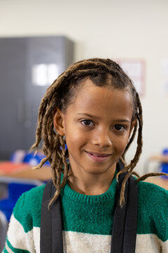 African American male child smiling, sitting at school wearing green sweater and backpack straps