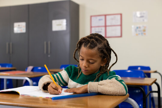 African American child boy writing in notebook at classroom desk with yellow pencil