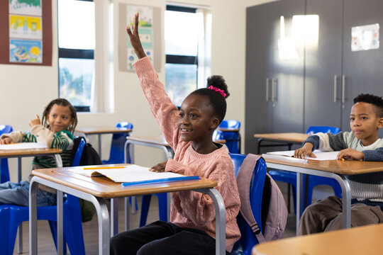 African American children sitting in class, girl in pink sweater raising hand with pencil