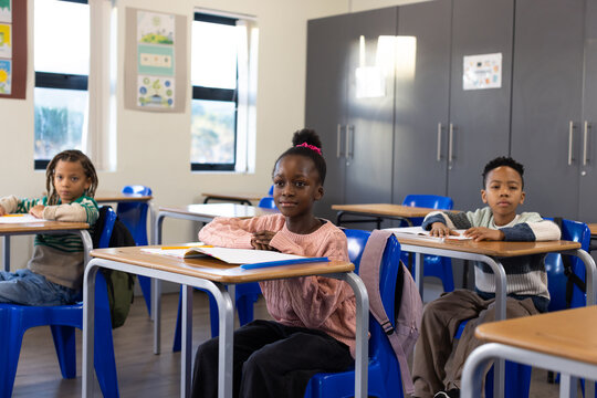 African American children sitting in classroom with girl in pink sweater using notebook and pencils
