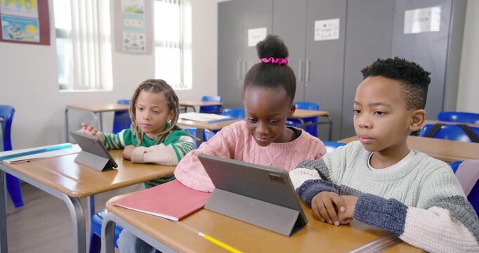 African American kids sitting at desks, center girl spotting tablet content, tapping to finish work