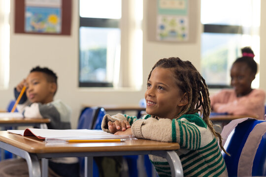 African American children sitting at desks in bright classroom with notebooks and pencils