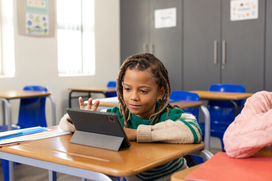 African American child sitting at school desk wearing green sweater using tablet on folio cover