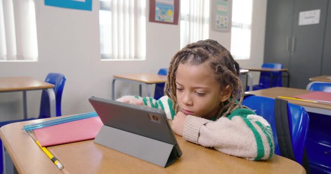 Male child in cream-striped sweater showing tiredness, reaching tablet on school desk, smiling