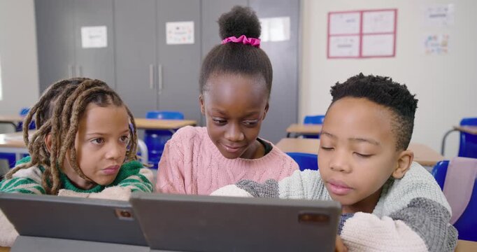 African American children prompted by tablets leaning in, tapping screens in classroom, smiling