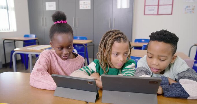 Elementary students noticing two tablets, tapping and leaning on desk, collaborating on classwork