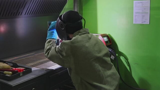 A student in a training workshop performs manual arc welding of metal in a protective mask during a practical lesson.