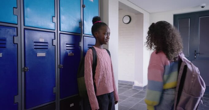 African preteen standing in pink sweater by blue school lockers, two peers pointing, covering face