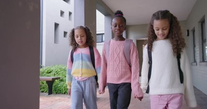 Diverse female preteens entering campus corridor holding hands walking to courtyard with backpacks