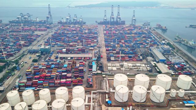 Jakarta, Indonesia - 18 July 2026: Aerial view of Port of Tanjung Priok with rows of colorful shipping containers, large storage tanks, and industrial cranes along the coastline.