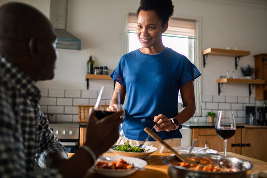 Smiling woman serving salad to partner in modern home kitchen