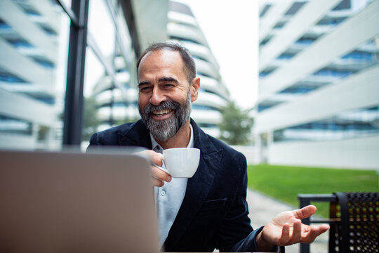 Smiling businessman on video call at outdoor cafe in modern office complex