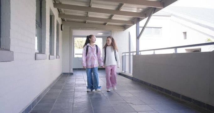African American preteen girls entering corridor, walking holding hands toward class with backpacks