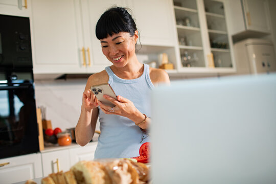 Smiling woman using smartphone in modern kitchen