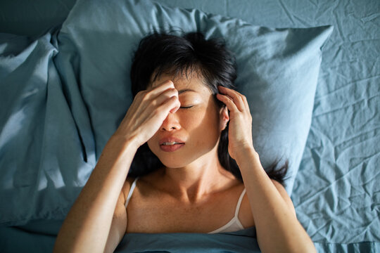 Woman in bed covering eyes in morning light