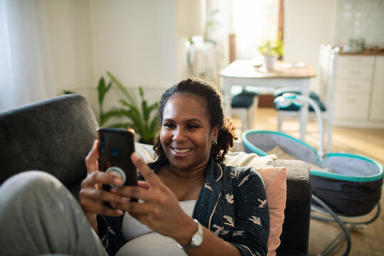 Pregnant woman using smartphone on sofa at home