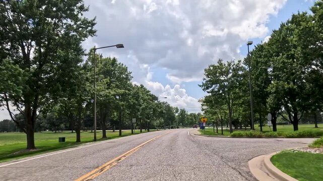 Vehicle point of view shot driving along a university campus road past student housing dormitories and directional signage, coming to a stop sign. Captured at University of Illinois Springfield.
