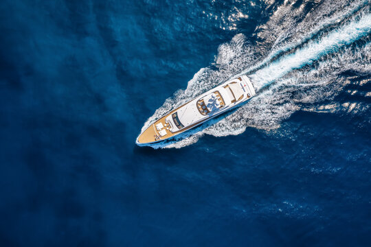 Aerial overhead view of a ultra modern luxury yacht cruising with high speed over blue ocean leaving a trail of surf and waves behind