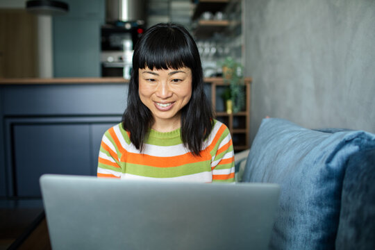 Smiling woman working on a laptop on living room sofa