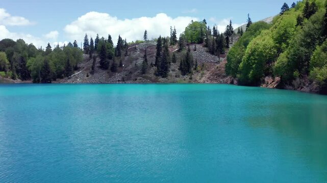 Turquoise Green Lake fills aerial view beside dense forest and lingering snow in Adjara, Georgia, supporting alpine tourism, outdoor travel, nature documentaries and destination marketing campaigns.