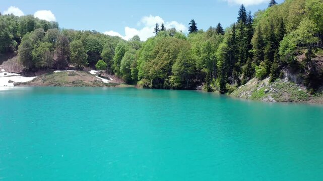 Alpine Green Lake fills aerial view beneath snow patches and mixed woodland in Khulo, Georgia, supporting mountain tourism, freshwater ecology, seasonal travel and environmental education media.